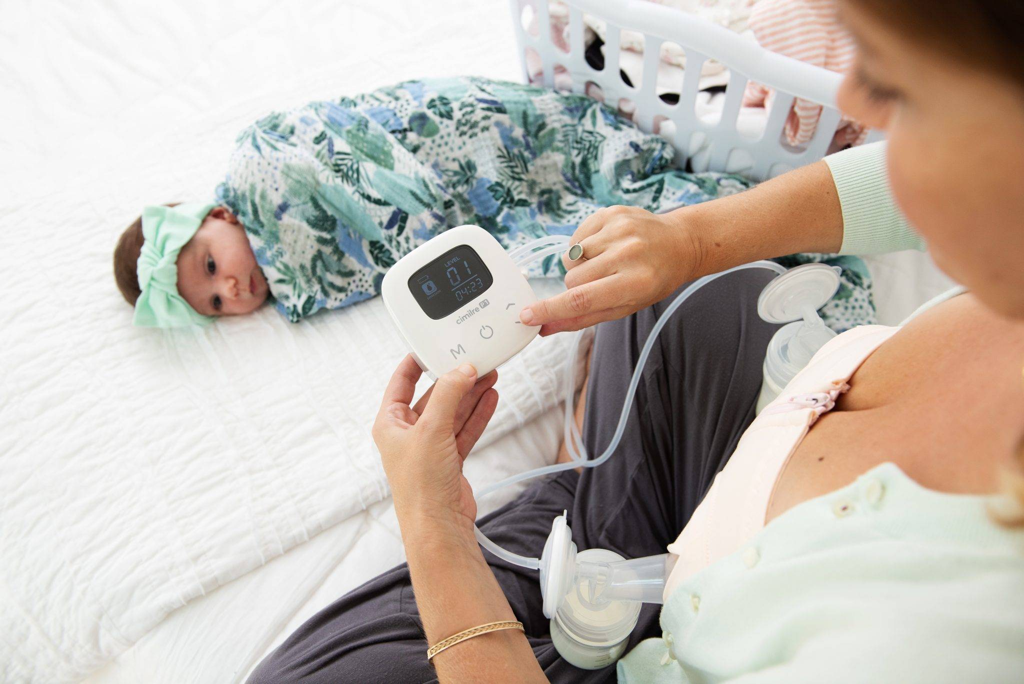 Person breast pumping on bed with baby and laundry